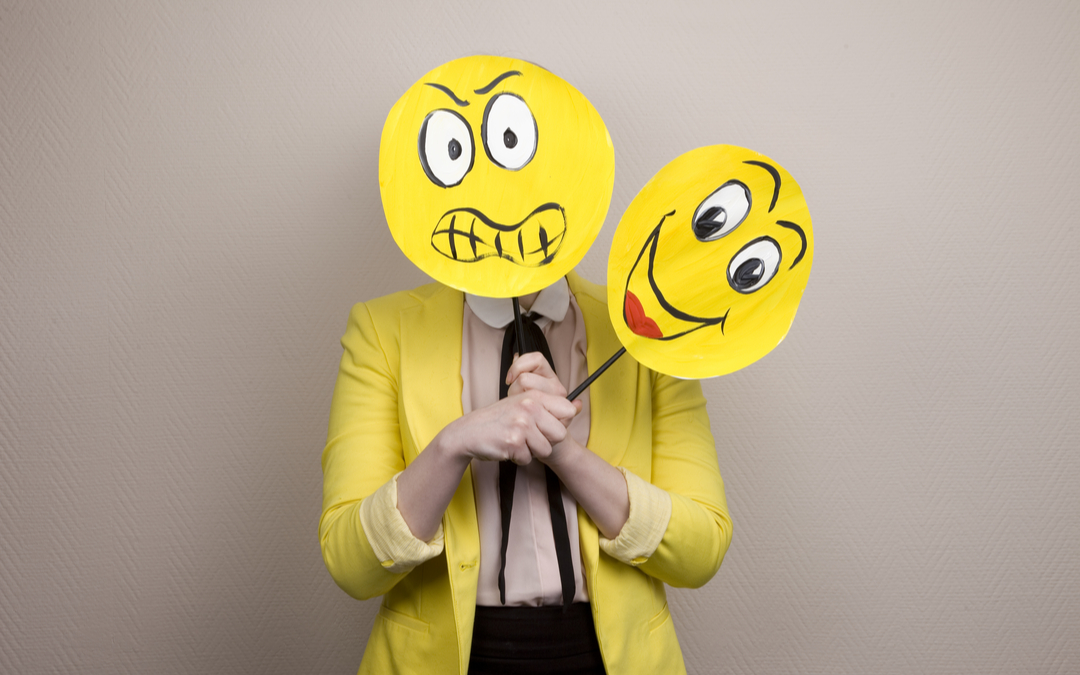Woman demonstrating concept of emotional intelligence by holding drawings of happy and sad faces
